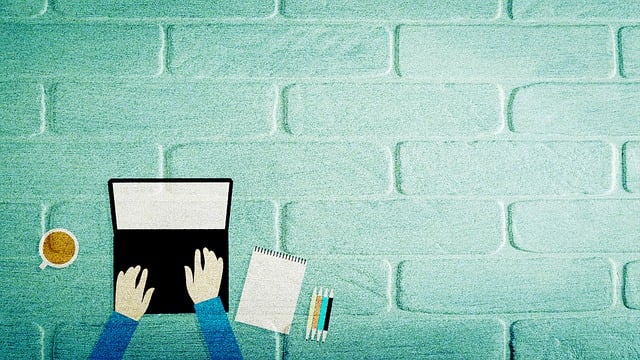 Image avec des bras de personne tapant sur un clavier d'ordinateur, avec un carnet et un café à côté.