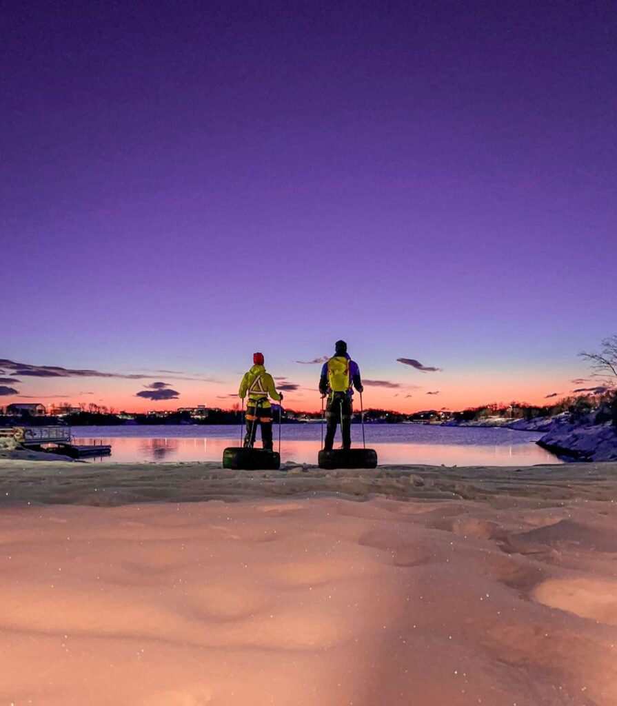 Deux amoureux aventuriers devant l'horizon la nuit, tractant des pneus sur la neige.