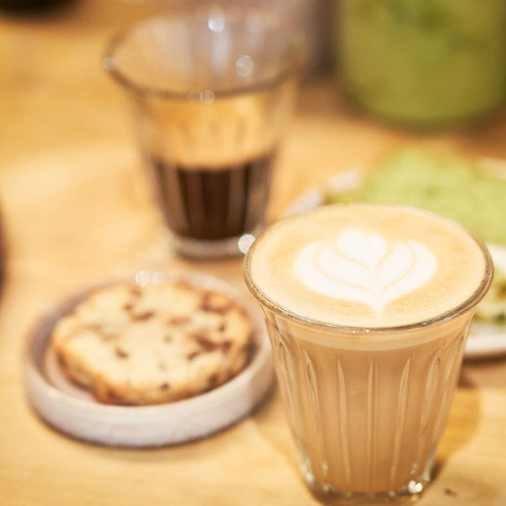 Deux cafés posés sur une table avec un cookie servie dans un récipient blanc.